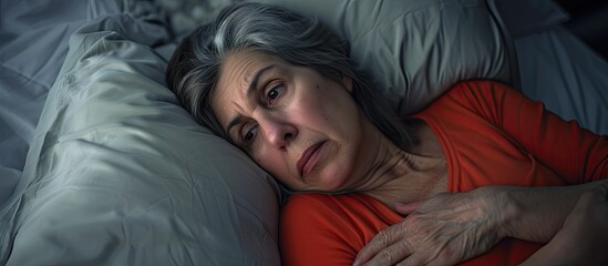 Middle aged woman sitting on bed feels unhealthy touch stomach suffers from severe crampy abdominal pain. with copy space image. Place for adding text or design