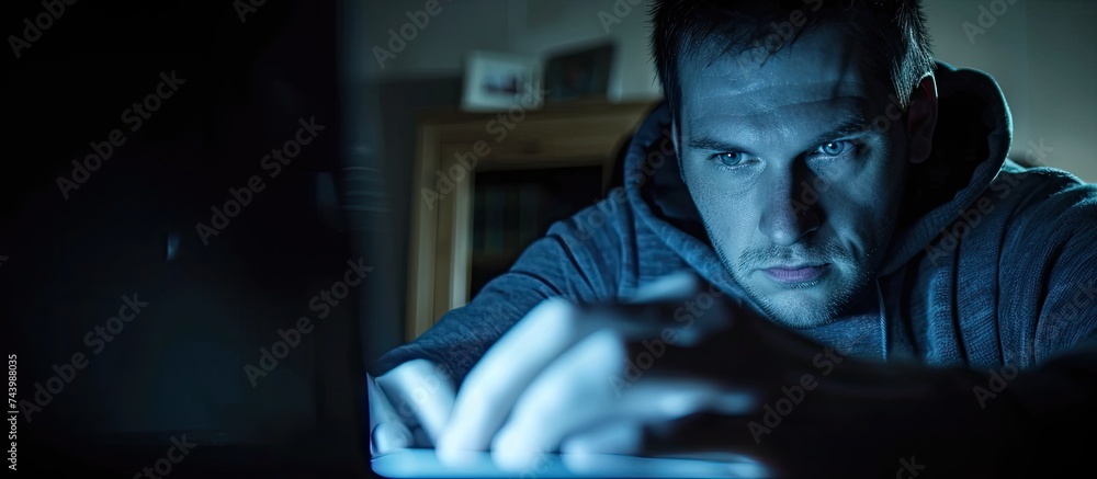 Fototapete Computer spy Side view of young man typing and looking at computer monitor while sitting at the table in dark room. with copy space image. Place for adding text or design