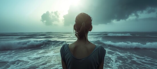 Posed image of an anonymous female staring out to sea in hope or in despair An enigmatic image suitable for International Womens Day or similar cause promotion. with copy space image - obrazy, fototapety, plakaty