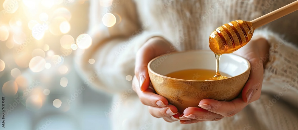 Aufkleber female hands holding a bowl of bee honey and a wooden spoon close up elaboration of organic soap bas