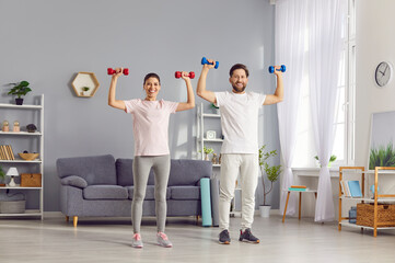 Young and positive family couple embraces a healthy lifestyle by workout sport training together at home. With dumbbells in hand, they focus on bicep, weightlifting fitness exercises.