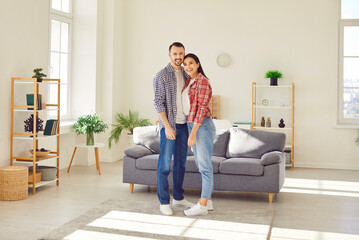 Full length portrait of a happy family couple stands together in cozy living room, embracing and sharing smiles. Joy, fun, and leisure, capturing the essence of togetherness in home.