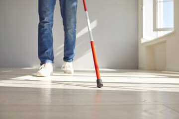 Cropped photo of legs of blind disabled man in casual clothes with long stick walking in empty room...