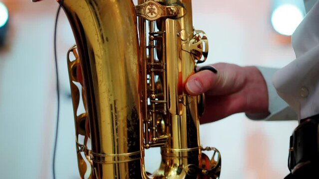 A saxophonist plays music at a concert indoors on stage. a golden saxophone in the hands of a male musician. Slow motion