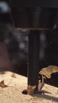Experience the artistry of woodworking as a drill effortlessly cuts through wood in mesmerizing 4K vertical slow motion, with wood dust and chips dancing in the air.