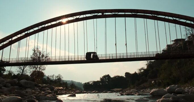 An auto-rickshaw traversing across a weathered iron bridge as the radiant sun illuminates the backdrop.