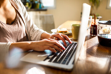 Cropped shot of a woman typing on laptop keyboard on kitchen table