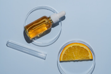 Dropper bottle with orange serum with vitamin C in a petri dish next to orange slice and a test tube. Laboratory cosmetics research, antioxidant testing. Skin care