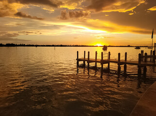 An image of a colorful sunset over the bay near Treasure Island, Floridia with a wooden dock in the foreground.