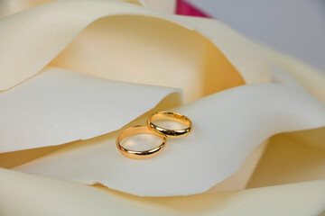 Wedding gold rings lie on the petal of a light yellow artificial rose.