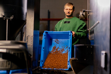 worker at a coffee factory pours green coffee from a blue box int a coffee roasting mechanism