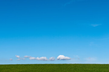 Fototapeta premium Small clouds over horizon over green grass hill