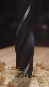 Explore the magic of timber craftsmanship in stunning 4K vertical slow motion, as a drill effortlessly penetrates wood, releasing clouds of wood dust and chips into the air.