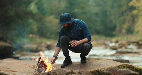 A traveler drinks tea from a metal mug near a campfire during a tourist hike in the mountains