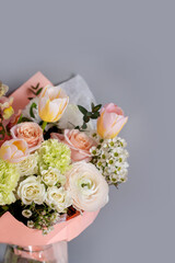 a delicate light bouquet of spring flowers of ranunculus , tulips, dianthus on a gray background with a place for text.