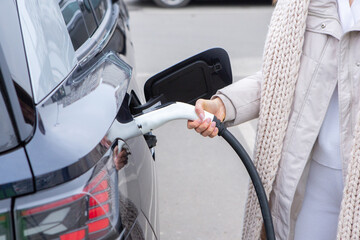 Young woman charging her electric car at a charging station in the city. Eco fuel concept. The...