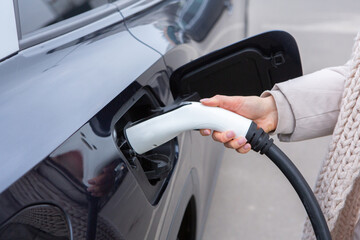 Young woman charging her electric car at a charging station in the city. Eco fuel concept. The...