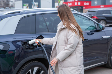 Young woman charging her electric car at a charging station in the city. Eco fuel concept. The...