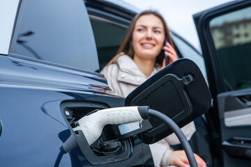 Young woman using a smartphone to pay for electric car at the charging station. Recharging battery from charging station.