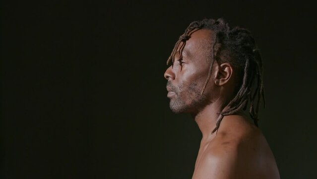 Man of African ethnicity turns toward the camera with a serious expression on a black backdrop