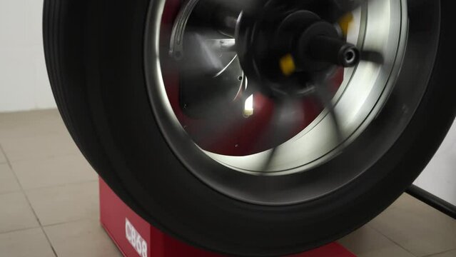 Tire balancing in motion on professional balancer equipment. Auto service tech optimizes wheel performance, precise calibration for smooth ride. Vehicle maintenance, workshop scene, spinning rim.