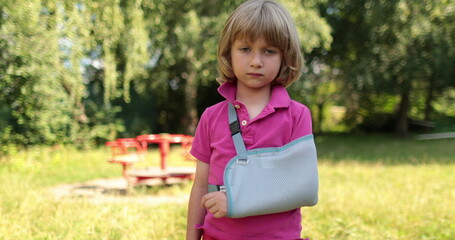 Sad child outdoors with a broken limb small, injured boy. The child has a broken arm. Bandage on the arm