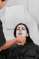 Relaxed brunette woman at the spa while being applied a white mask.