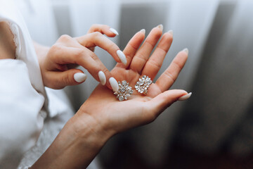 The bride holds in her hands and shows her earrings with precious stones, close-up. Morning of the...