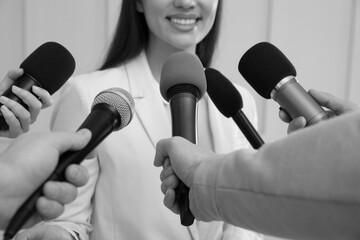 Businesswoman giving interview to journalists indoors, closeup. Black and white effect