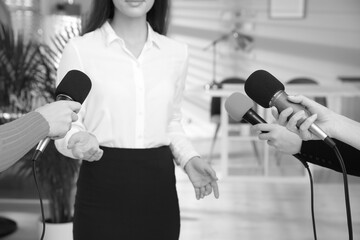 Businesswoman giving interview to journalists indoors, closeup. Black and white effect