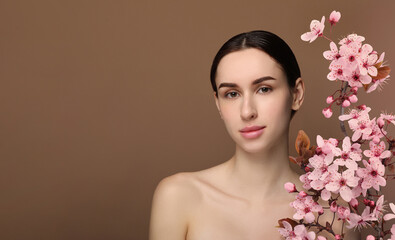 Naklejka premium Beautiful woman with smooth skin and flowers on brown background. Space for text