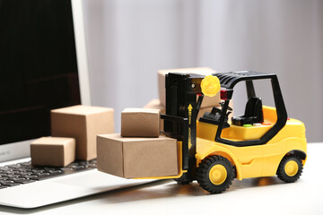 Toy forklift with boxes near laptop on table. Logistics and wholesale concept