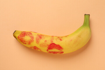 Banana with red lipstick marks on pale orange background, top view. Sex concept