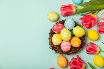 Fototapeta na wymiar Easter eggs with a bouquet of tulips on a bright turquoise background. Easter celebration concept. Colorful easter handmade decorated Easter eggs. Place for text. Copy space.