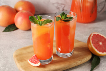 Tasty freshly made grapefruit juice, fruits and mint on light grey table