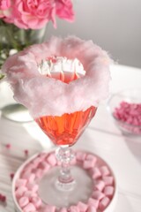 Cotton candy cocktail in glass and marshmallows on white table, closeup