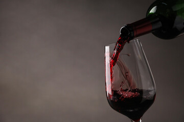 Pouring tasty red wine from bottle into glass on gray background, closeup. Space for text