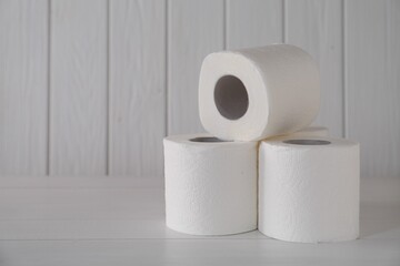 Many soft toilet paper rolls on white wooden table. Space for text