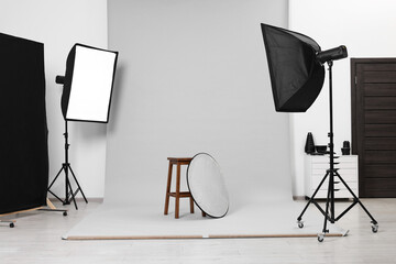 Stool with light reflector surrounded by professional lighting equipment in photo studio - obrazy, fototapety, plakaty