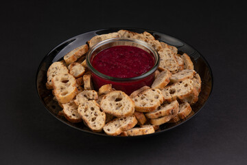 bowl of red sauce with bread toasts placed on a white plate isolated on a black background