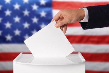 Fototapeta na wymiar Election in USA. Man putting his vote into ballot box against national flag of United States, closeup