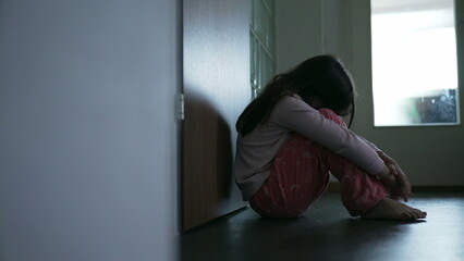 Struggling child sitting on corridor floor covering face feeling loneliness and solitude during...