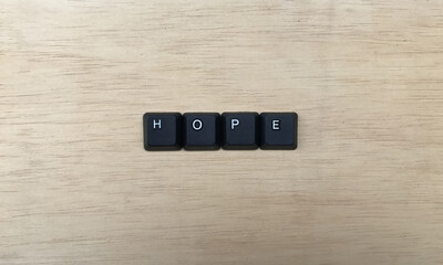 The word HOPE written with black computer keys on wooden background.