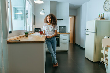 Young woman in kitchen with glass of wine looking at camera