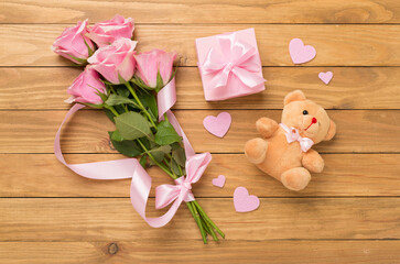Obraz na płótnie Canvas Pink roses with hearts and gift box on wooden background, top view.