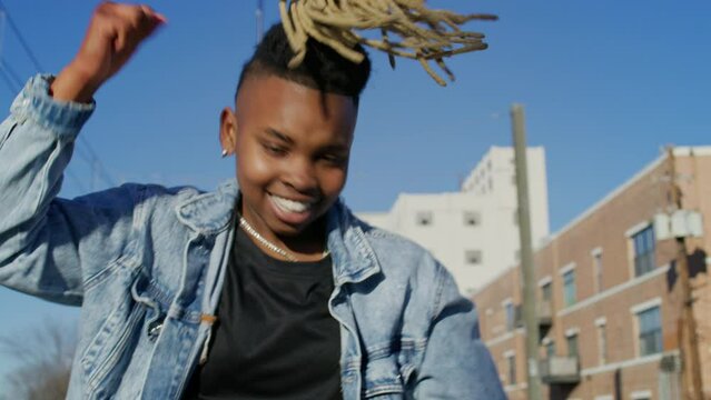 Medium shot of a non-binary person with blonde dreadlocks dancing in an urban area
