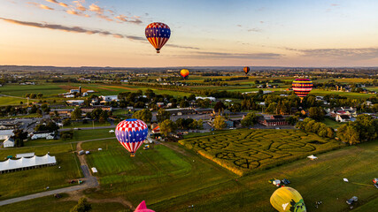An Aerial View of Multiple Hot Air Balloons Soar Over A Picturesque Landscape Featuring A Corn...