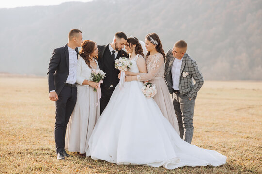Wedding photo session in nature. The bride and groom kiss and their friends