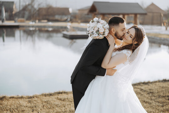 A young bride and groom tenderly embrace in the rays of the autumn sun. Tender and beautiful young girl bride. A man kisses his beloved. Against the background of a beautiful garden