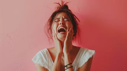 Fotobehang Portrait of a young woman screaming in frustration with hands on face against a pink background. © Another vision